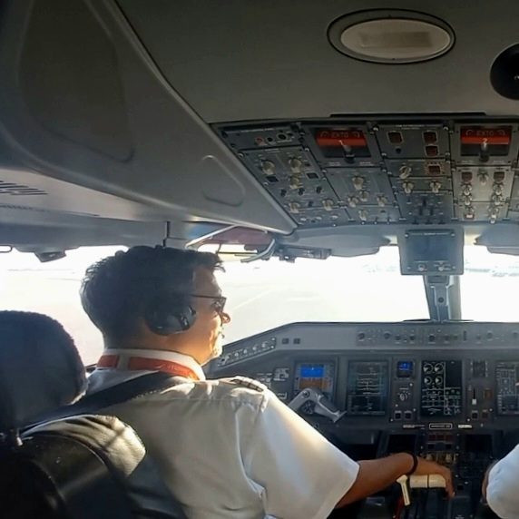 Keep the sunny side up! ;-) Mann mit Headset und Sonnenbrille im Cockpit eines Flugzeugs, lächelt.